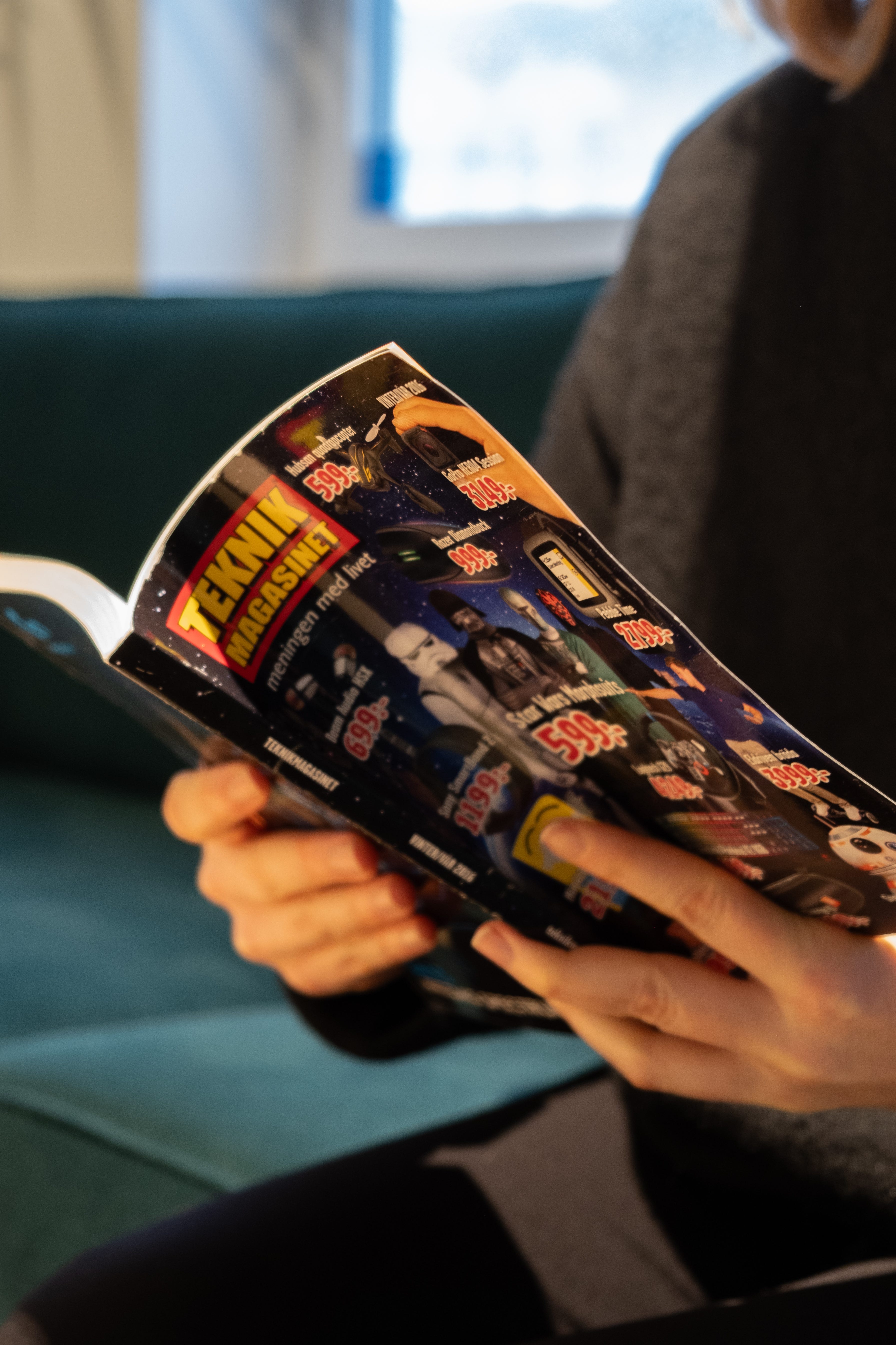 Person sitter i en soffa och bläddrar i en Teknikmagasinet reklamkatalog med teknik- och elektronikprodukter.